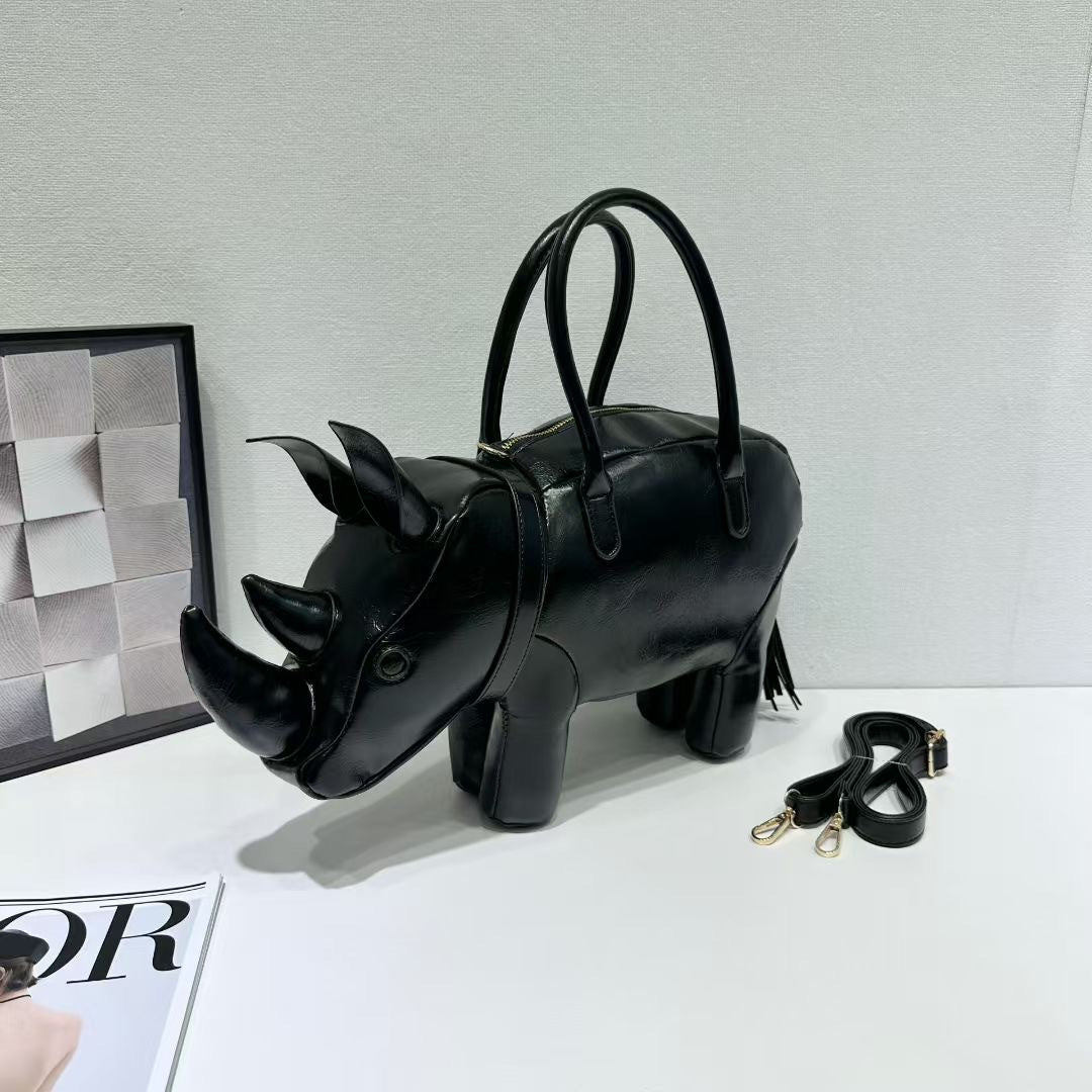 Rhinoceros-shaped 3D structured handbag with sculpted horns, four legs, tassel tail, twin top handles, and detachable, detail