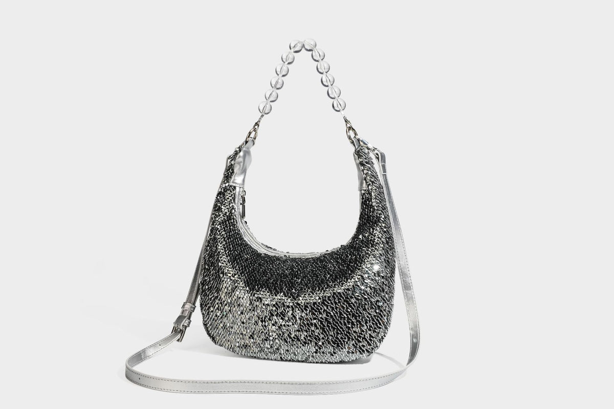 Kleine sichelförmige Schultertasche mit vollständig mit silberfarbenen Pailletten besetzter Außenseite, transparentem Henkel aus kugelförmigen Perlen und Reißverschluss in Silberoptik
