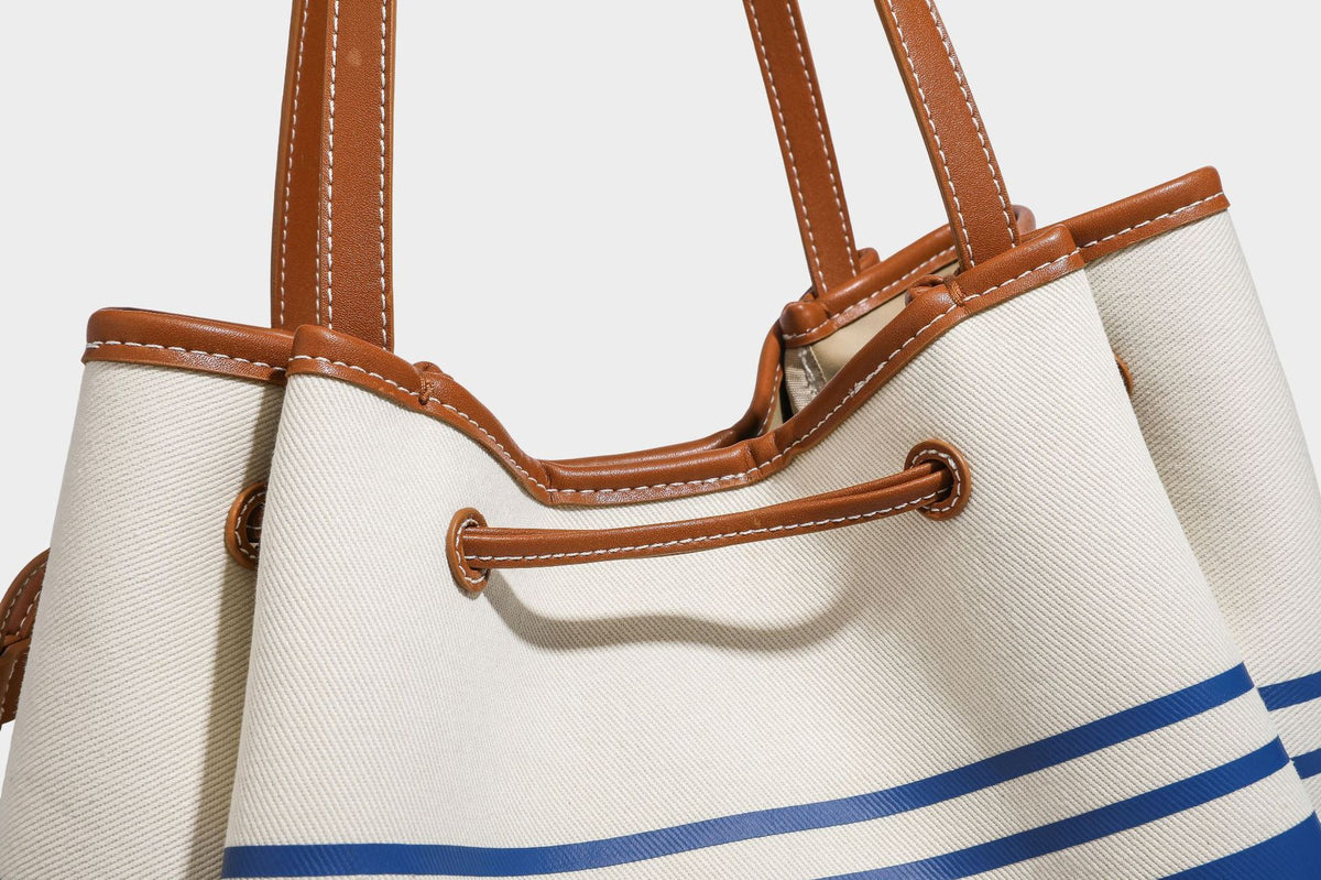 Large cream and navy striped canvas bucket tote bag with tan leather-look trim, drawstring closure, and double shoulder