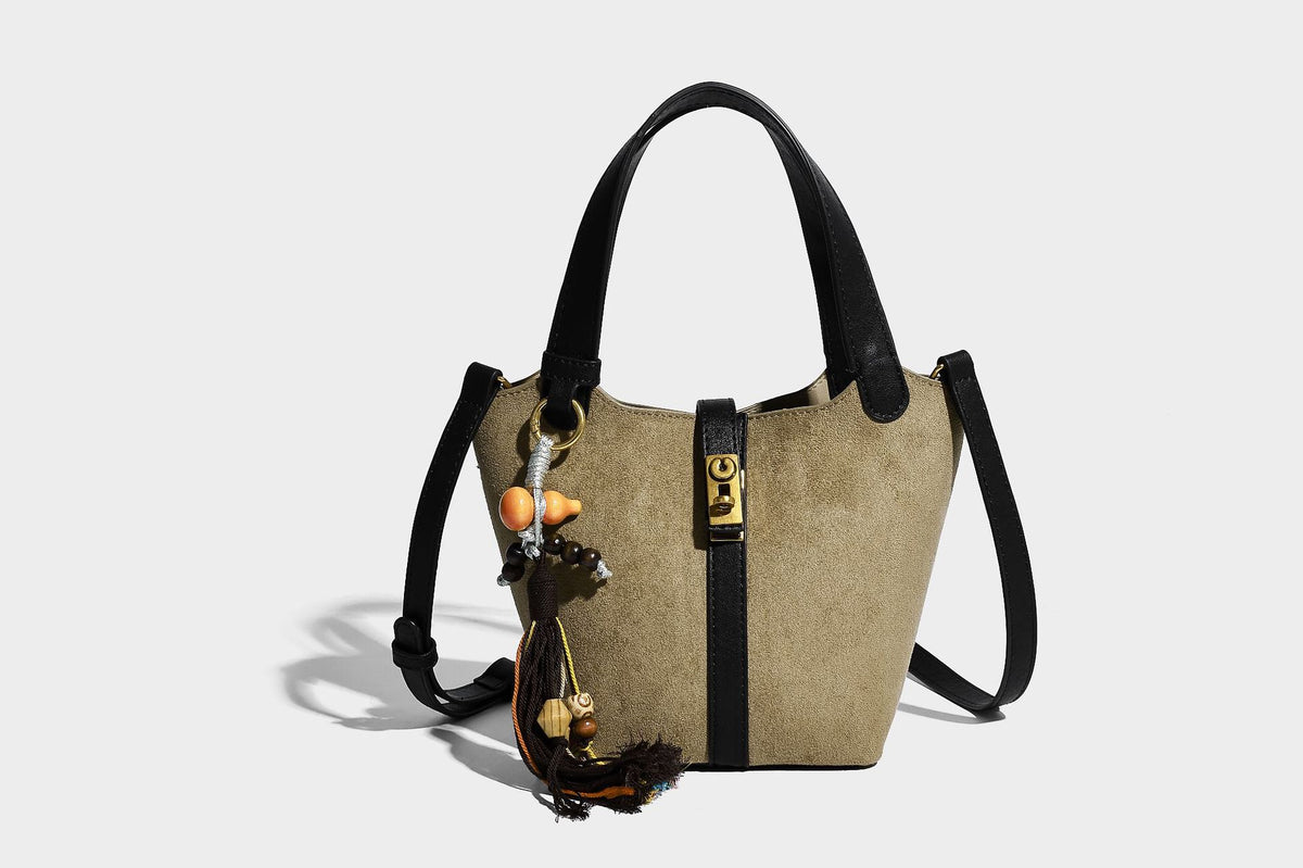 Small structured trapezoid tote bag in matte suede-look finish with black contrast trim, gold-tone front clasp, tassel charm