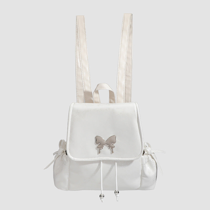 Compact white pearlescent flap backpack with silver-tone bow hardware and drawstring closure, detail view 2