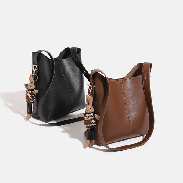 Smooth leather-look bucket bag with long flat shoulder strap, open top, gold-tone hardware, and decorative rabbit charm