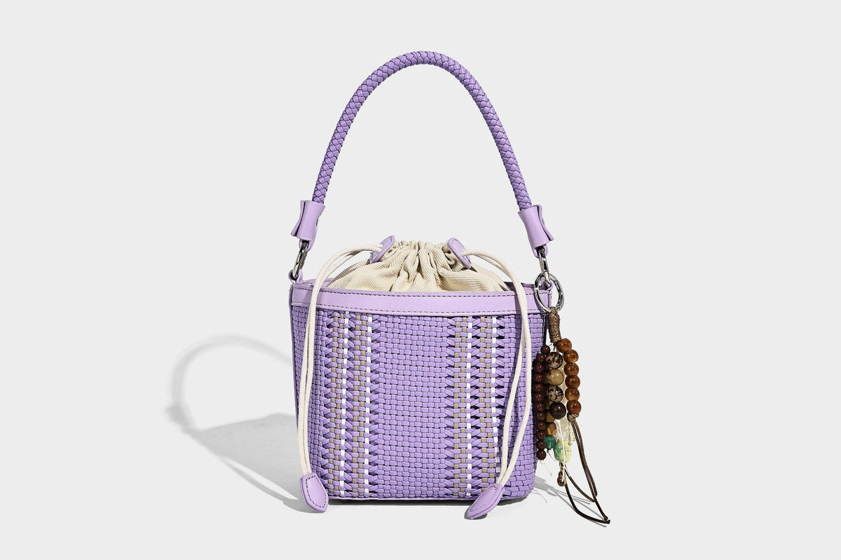 Small woven bucket bag with drawstring top, braided handle, detachable crossbody strap, and silver-tone ring hardware, detail