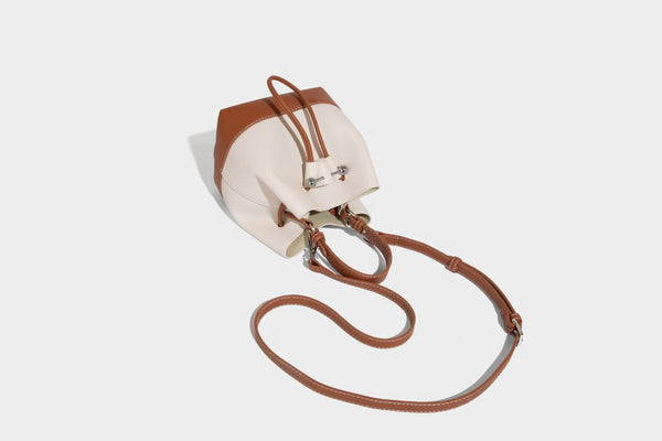 Small two-tone pebbled drawstring bucket bag with tan contrast base, metal toggle hardware, short top handle, and detachable