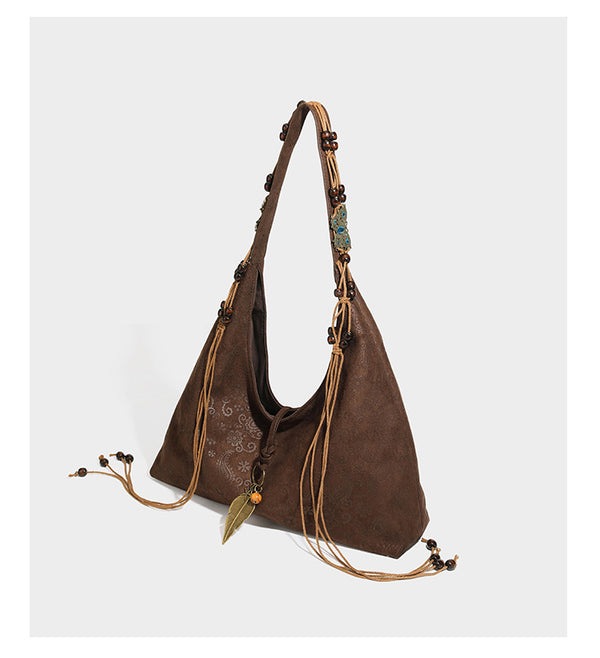 Slouchy boho hobo shoulder bag in embossed brown suede-look finish with beaded strap, cord tassels, and brass-tone leaf