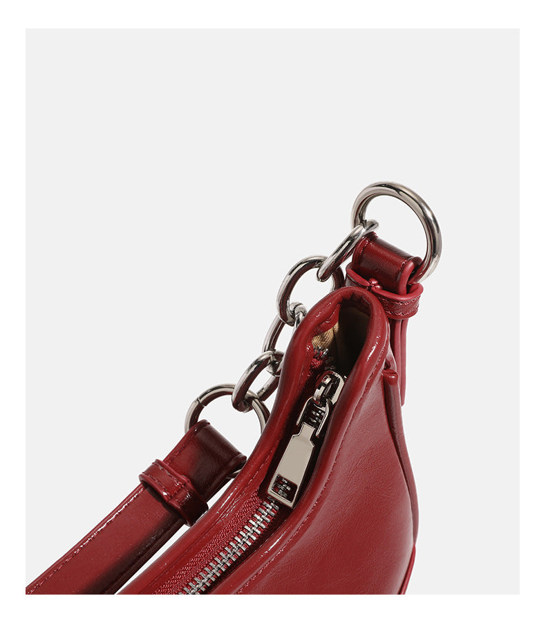 Compact crescent hobo shoulder bag in glossy burgundy leather-look finish with silver chain strap, red and green bead tassel