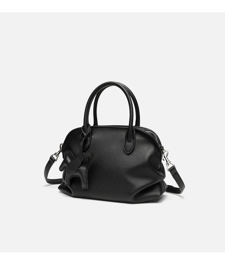 Rounded dome shell handbag in pebbled leather-look finish with twin top handles, zip closure, decorative horse charm, and