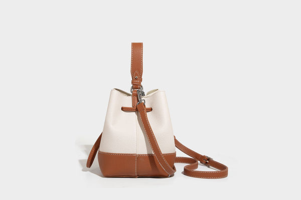 Small two-tone pebbled drawstring bucket bag with tan contrast base, metal toggle hardware, short top handle, and detachable