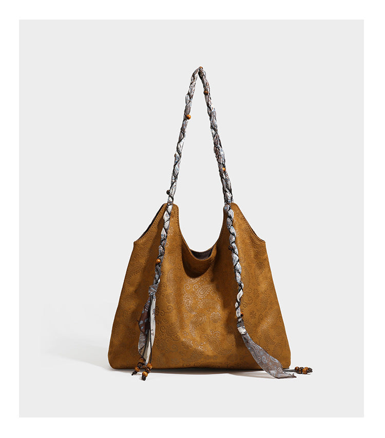 Slouchy paisley-embossed suede-look shoulder tote bag with braided patterned fabric straps and wood bead accents, detail view