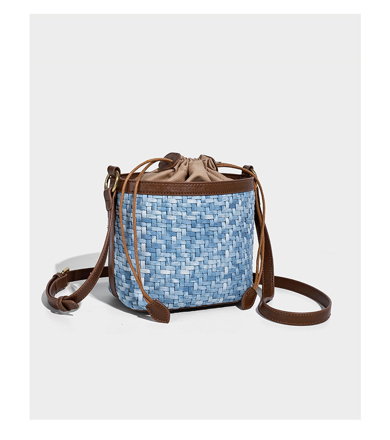 Small light blue woven bucket bag with brown leather-look trim, braided top handle, brass-tone ring hardware, drawstring