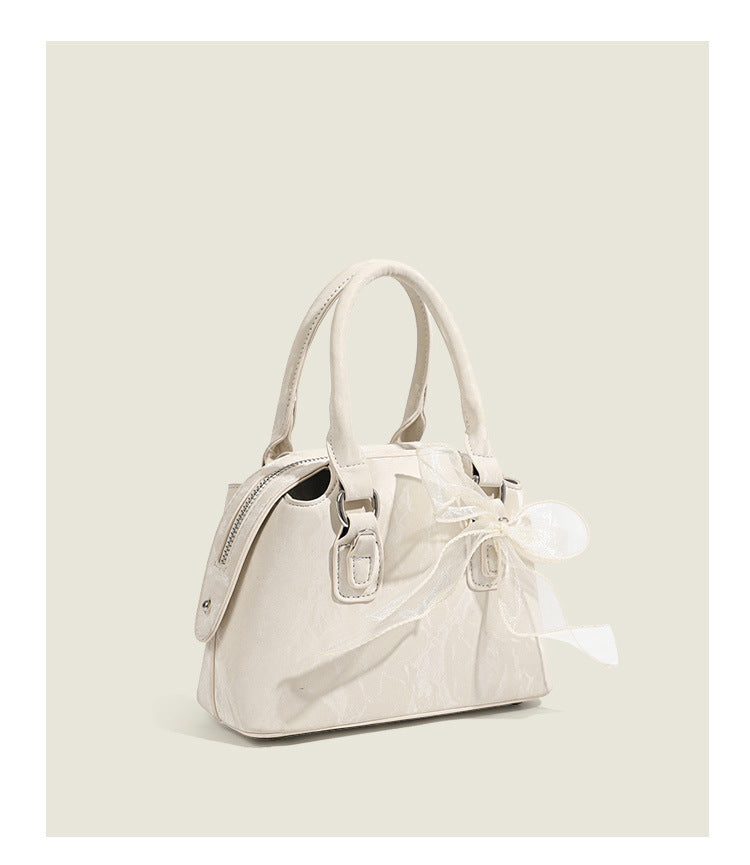 Small structured Boston bag in cream with glossy crinkled finish, sheer bow accent, silver-tone hardware, dual top handles
