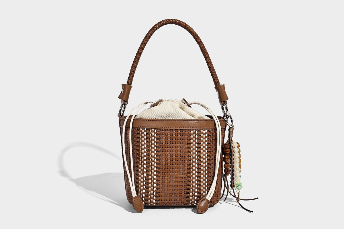 Small woven bucket bag with drawstring top, braided handle, detachable crossbody strap, and silver-tone ring hardware, detail