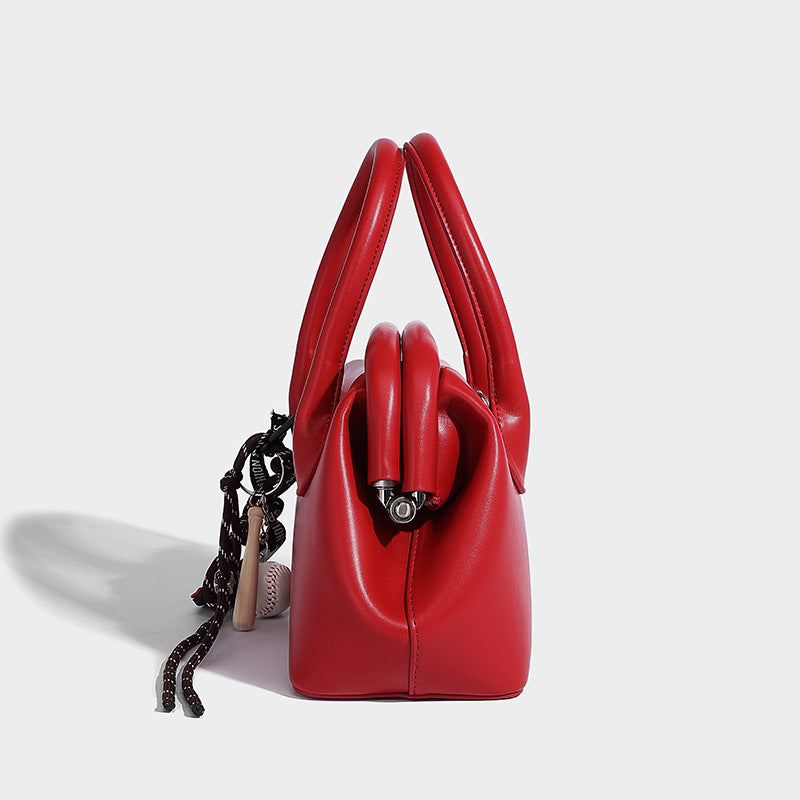 Small structured shell top-handle bag in red with heart charm and braided cord detail, smooth leather-look finish, detail