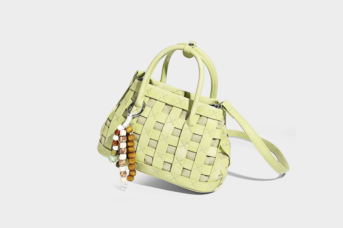 Small structured woven satchel tote with rounded top handles, silver-tone ring hardware, and bead tassel charm, detail view