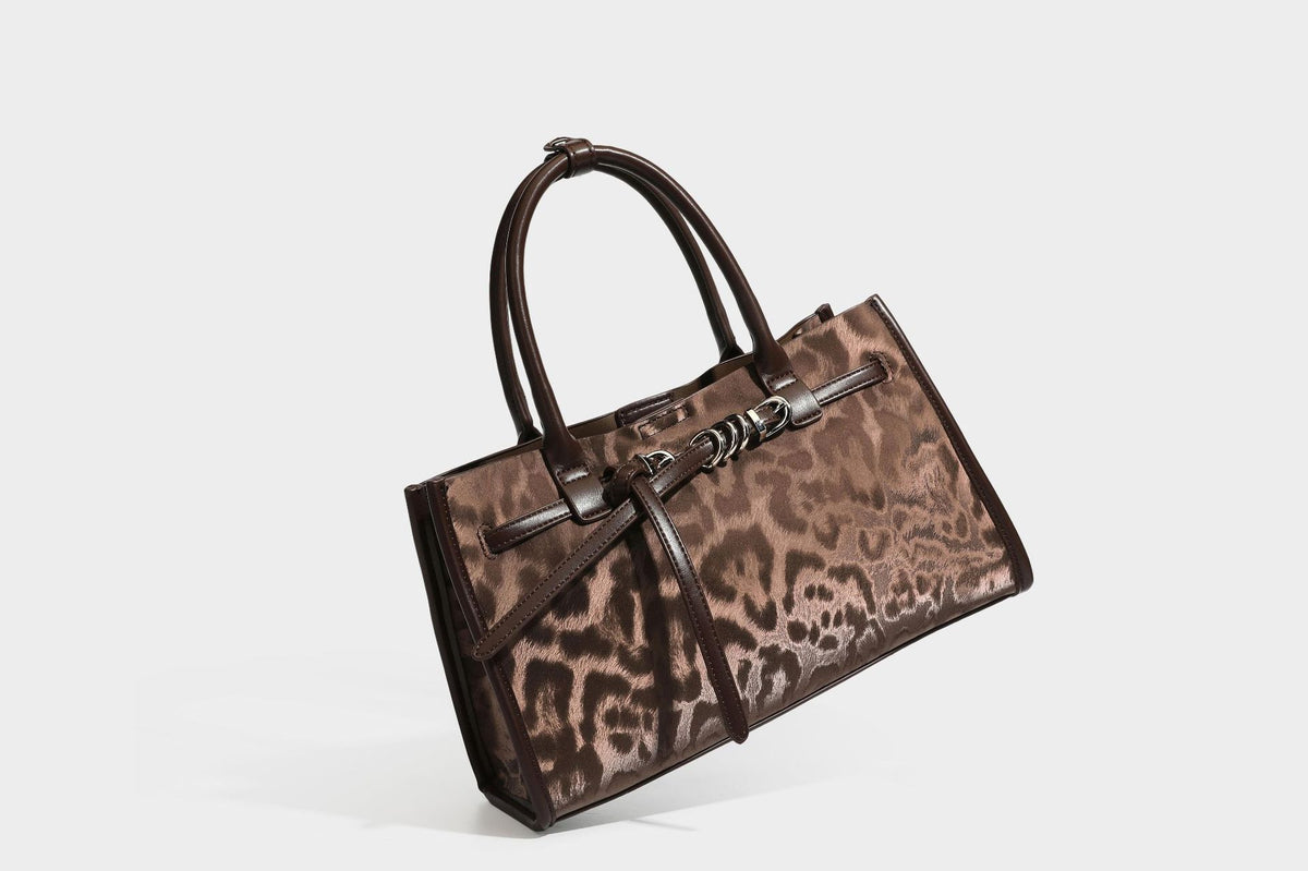 Structured leopard-print tote bag with glossy satin-like finish, dual rounded top handles, silver buckle-and-ring front