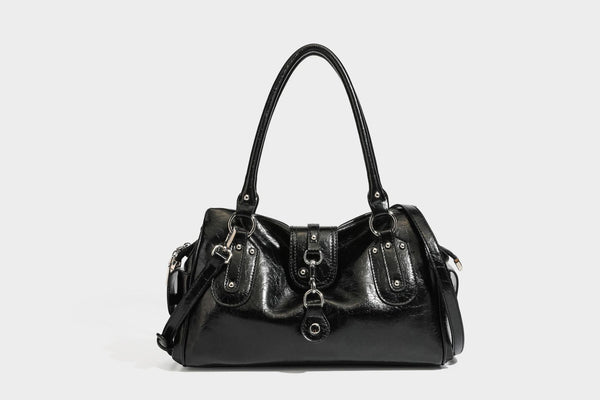 Glänzende, geknautschte Barrel-Satchel mit zwei oberen Tragegriffen, vorderem Klappen-Riemen-Panel, Ring- und Nietenbeschlägen sowie einem abnehmbaren