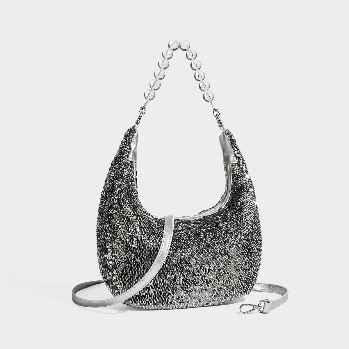 Small crescent shoulder bag with all-over silver sequin exterior, clear spherical bead top handle, and silver-tone zip, front