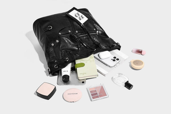 Glossy black convertible bucket backpack with silver grommet-studded straps, drawstring cinch closure, and front zip pocket