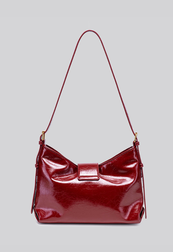 Glossy burgundy leather-look shoulder bag with curved gold-tone bar front closure, crinkled oil-wax texture, and adjustable