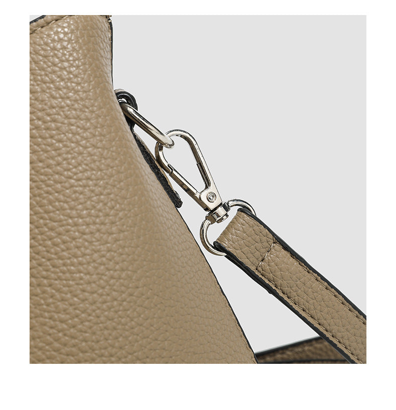 Structured taupe pebbled-texture bucket bag with top handle, silver ring hardware, tab-and-button closure, and knit bunny