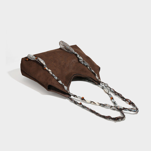 Slouchy paisley-embossed suede-look shoulder tote bag with braided patterned fabric straps and wood bead accents, detail view