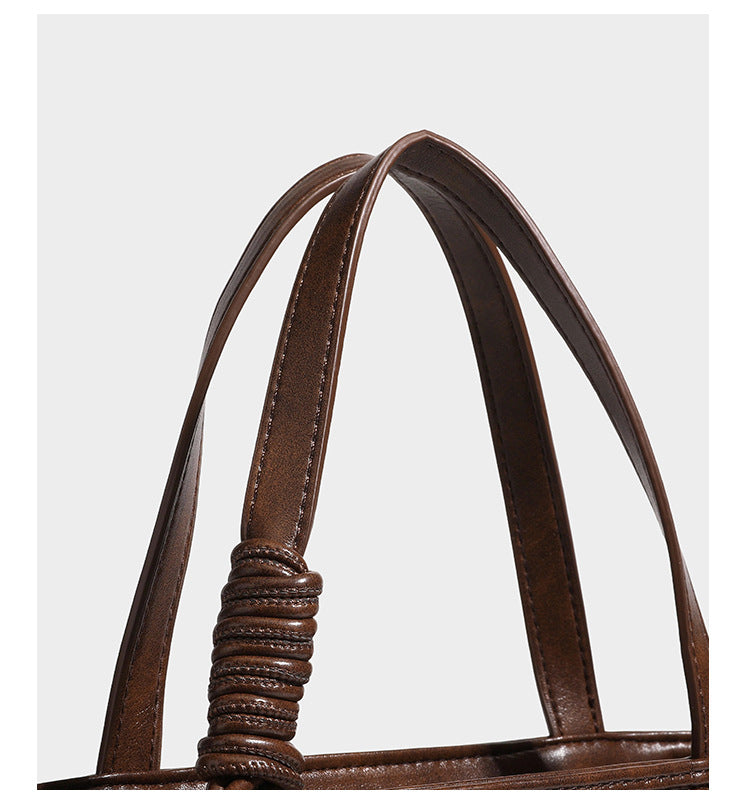 Strukturierte Tote Bag mit gewebter Oberfläche in Braun, goldfarbenen Metalldetails, seilumwickelten Tragegriffen, einer kleinen Fronttasche und weiteren Details