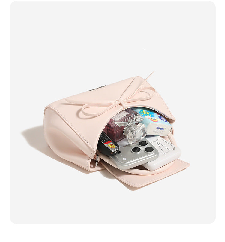 Structured mini trapezoid top-handle crossbody bag with sculpted bow front detail, smooth matte finish, silver-tone hardware