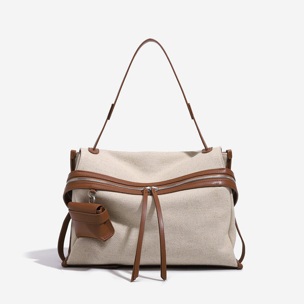Cream canvas zip-top shoulder bag with cognac leather-look trim, dual zipper, attached mini pouch, and tassel strap ties