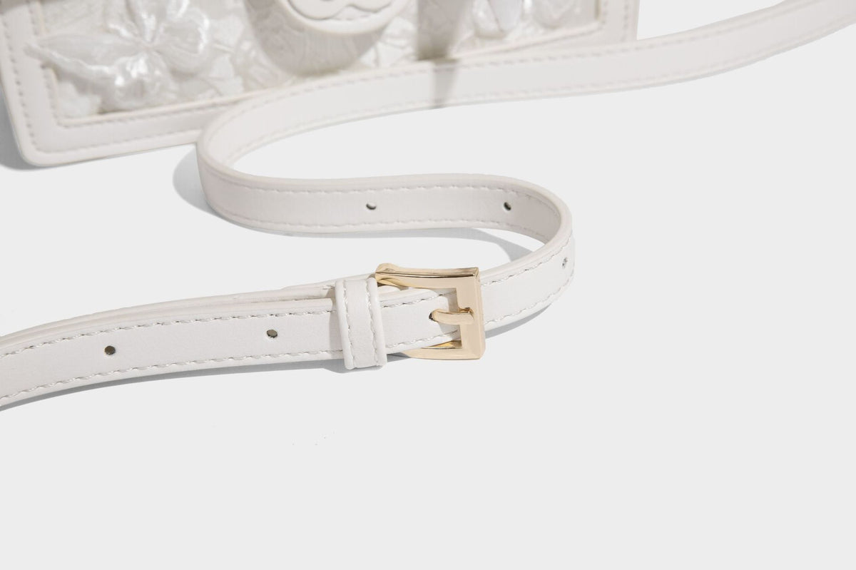 Small structured white flap bag with butterfly embroidery, flower-shaped turn-lock clasp, braided top handle with scarf bow