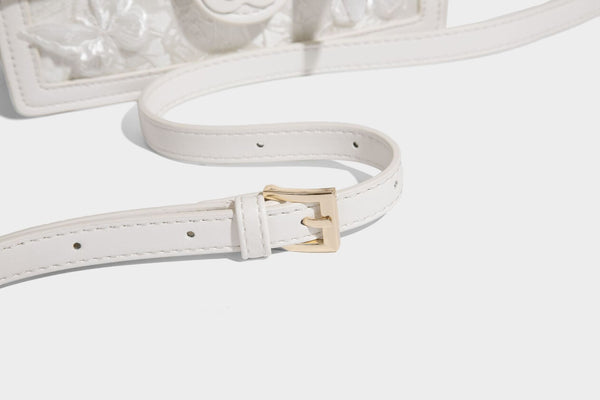 Small structured white flap bag with butterfly embroidery, flower-shaped turn-lock clasp, braided top handle with scarf bow