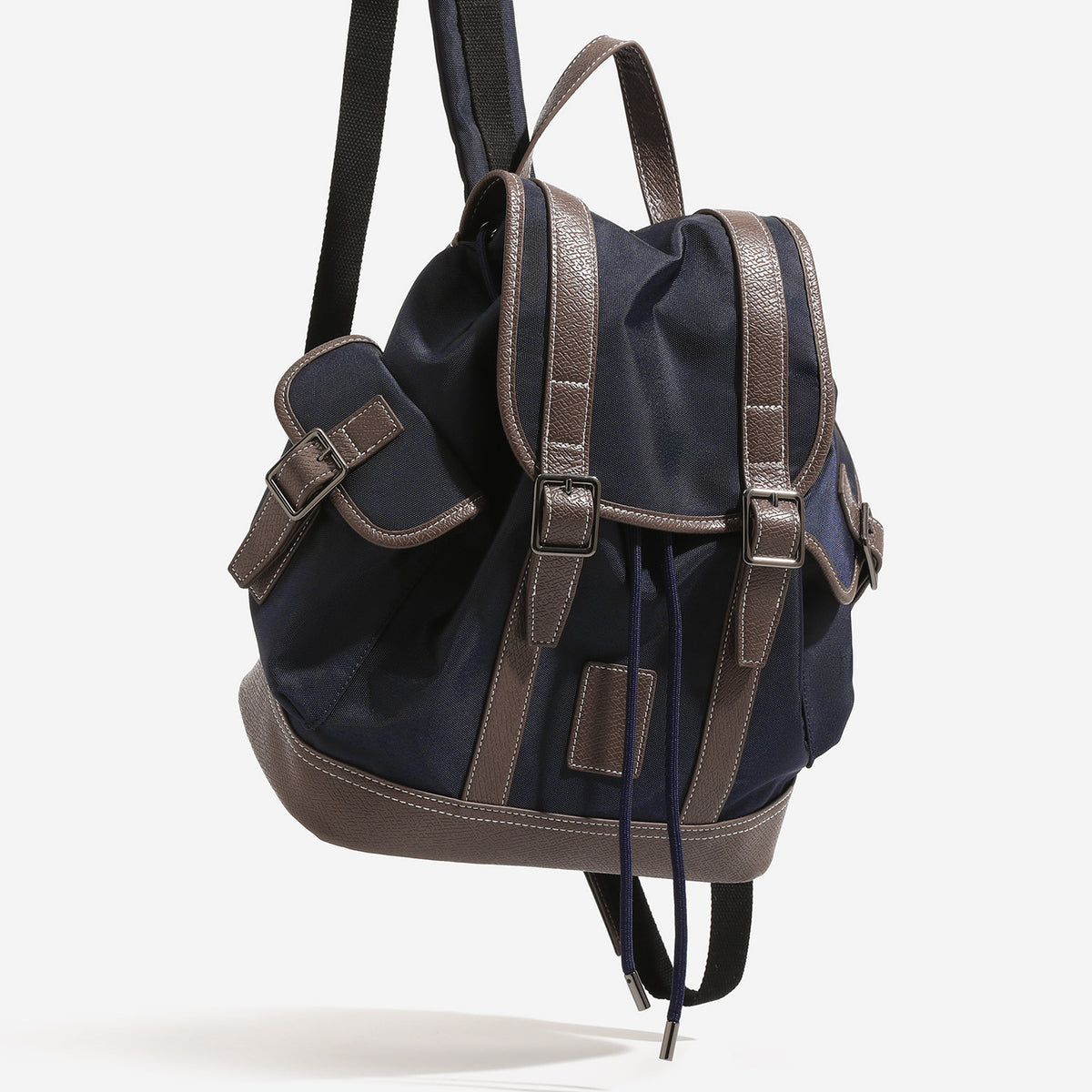Deep navy canvas backpack with brown textured leather-look trim, drawstring flap closure, buckle-strap front detail, and