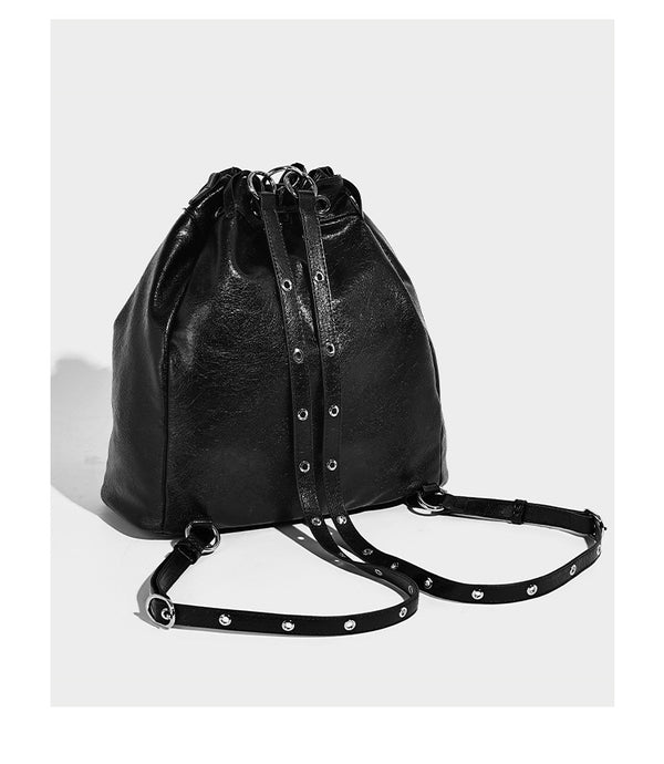Glossy black convertible bucket backpack with silver grommet-studded straps, drawstring cinch closure, and front zip pocket
