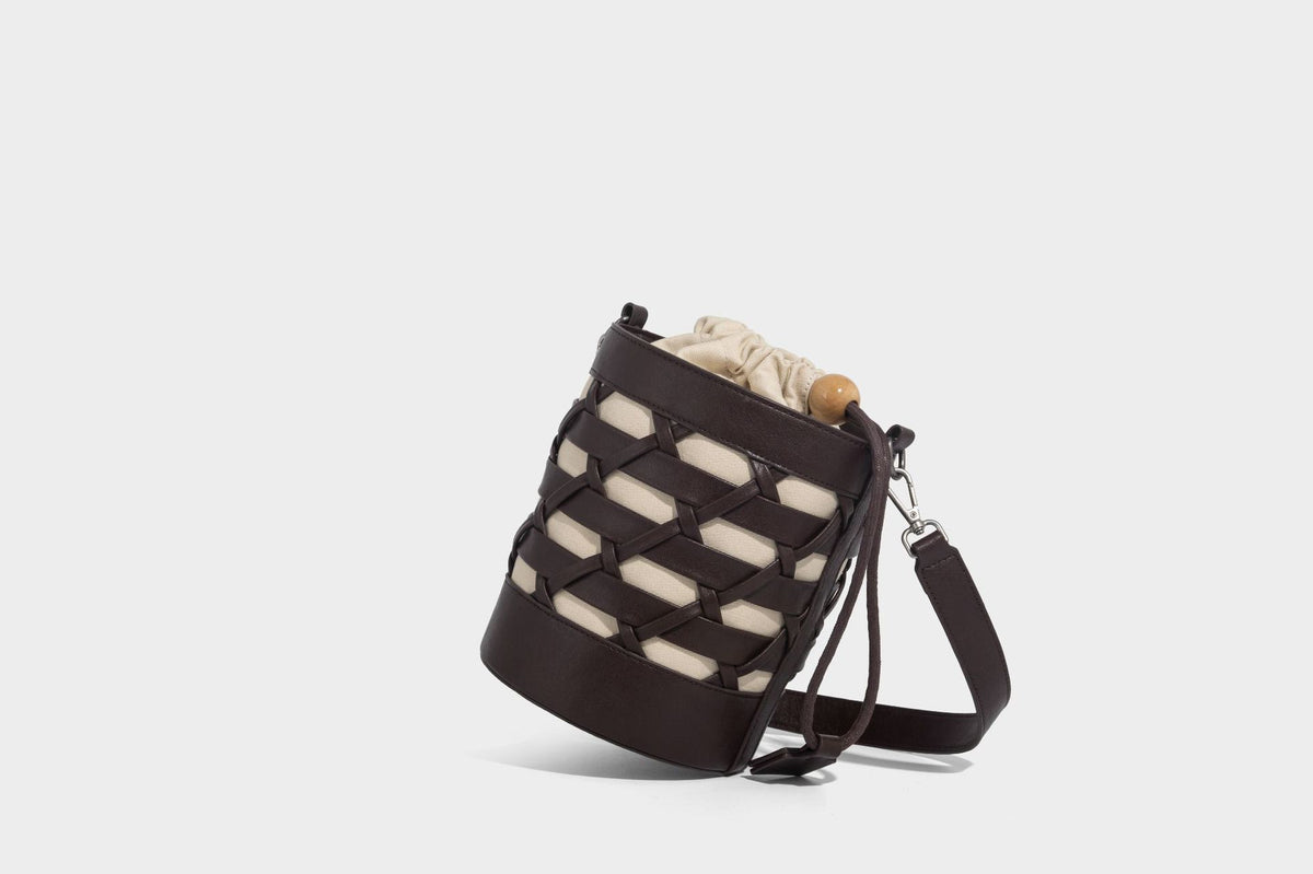 Small cylindrical woven lattice bucket bag with leather-look black trim, beige canvas body, wooden bead drawstring closure