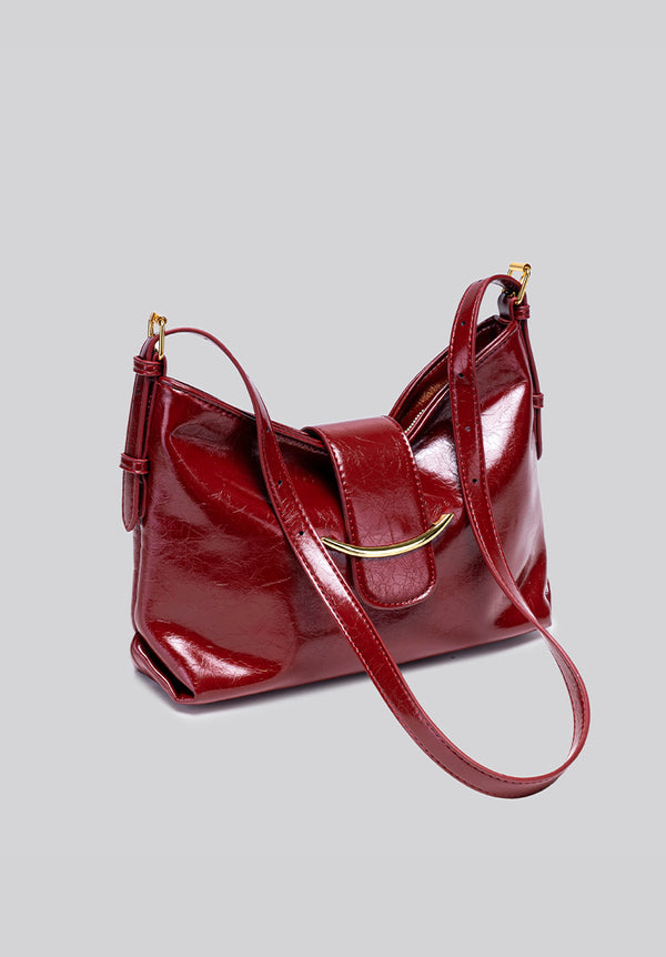 Glossy burgundy leather-look shoulder bag with curved gold-tone bar front closure, crinkled oil-wax texture, and adjustable