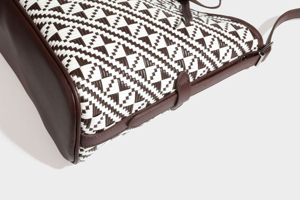 Woven geometric bucket shoulder bag in white and dark brown two-tone pattern with leather-look trim and drawstring top