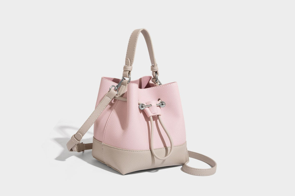 Small two-tone pebbled drawstring bucket bag with tan contrast base, metal toggle hardware, short top handle, and detachable