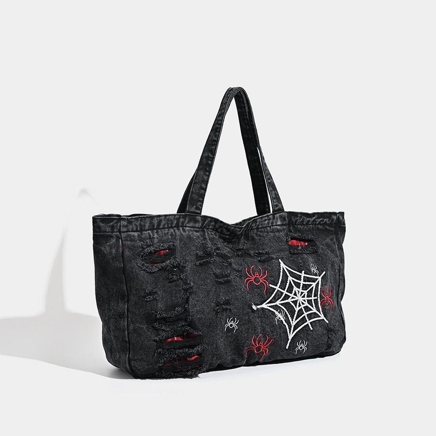 Large washed black distressed denim tote bag with white spider web embroidery and red spider motifs on the front panel