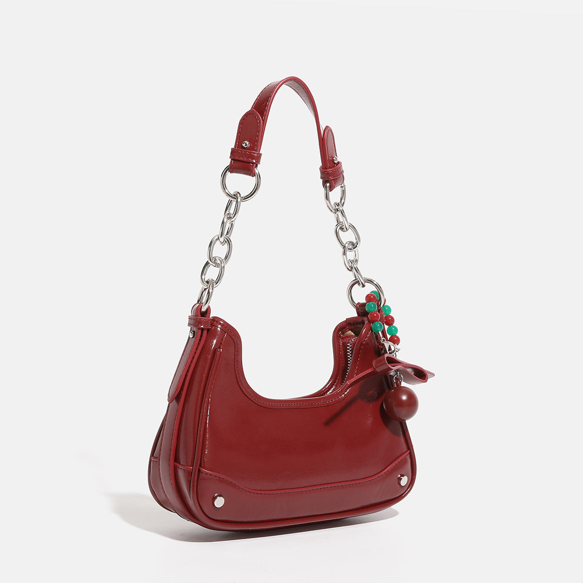 Small glossy cherry red crescent shoulder bag with silver chain strap, bead and tassel charm, and round pendant, front view
