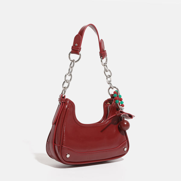 Small glossy cherry red crescent shoulder bag with silver chain strap, bead and tassel charm, and round pendant, front view