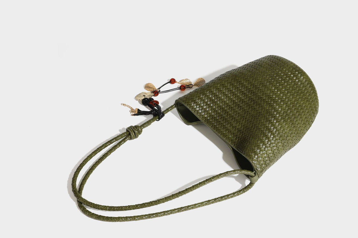 Olive green woven leather-look bucket bag with braided crossbody strap, knotted adjustment, and gold-tone tassel charm with