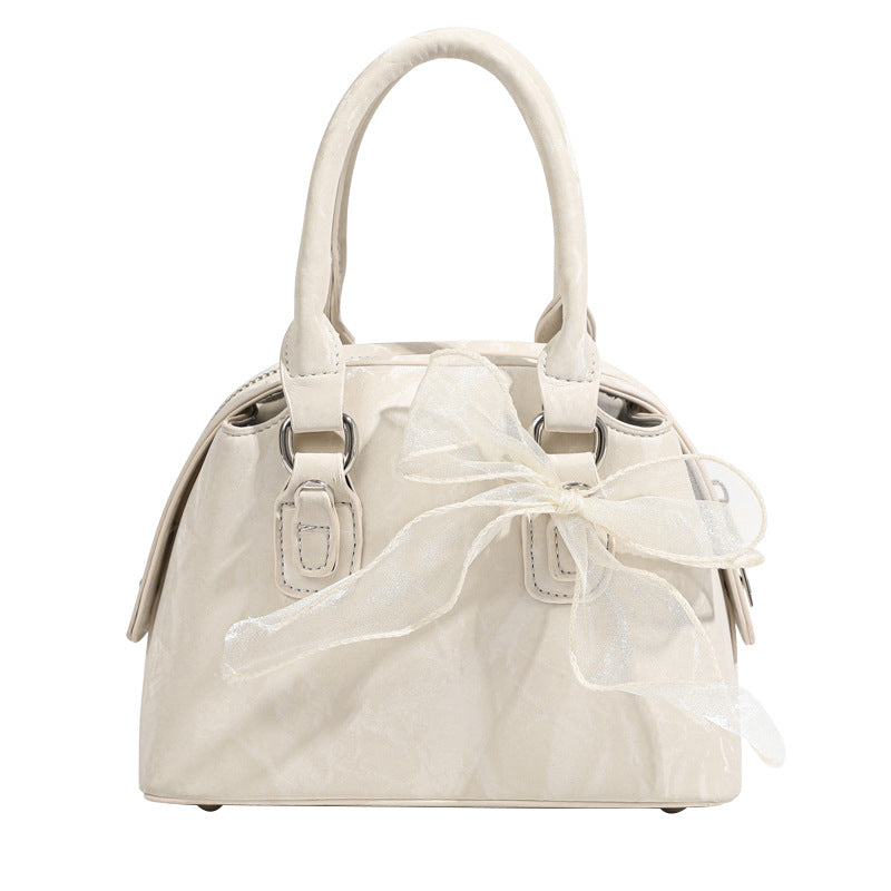 Small structured Boston bag in cream with glossy crinkled finish, sheer bow accent, silver-tone hardware, dual top handles