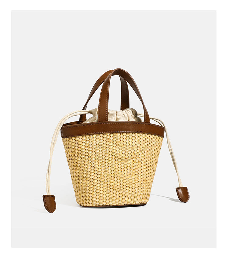 Kleine geflochtene Bucket Bag aus Stroh mit schwarzem Besatz in Lederoptik, zwei oberen Tragegriffen, cremefarbenem Futter mit Kordelzug und seitlichen Kordelverschlüssen