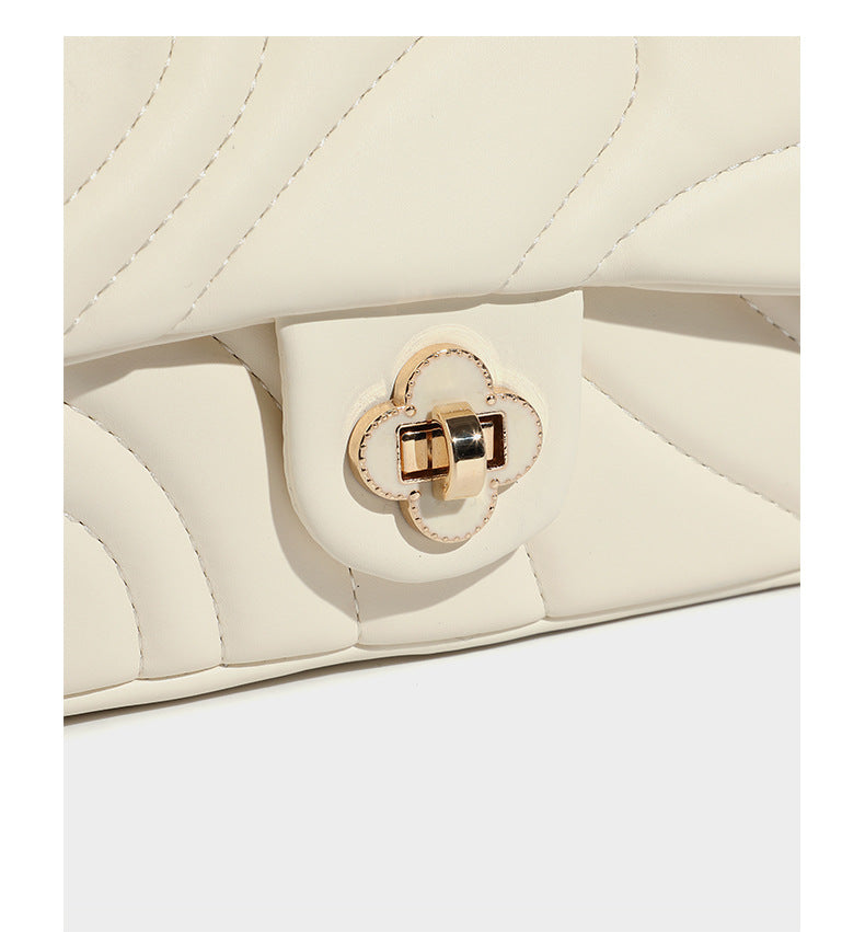 Compact cream quilted flap crossbody bag with wave stitching, gold-tone chain strap, and four-petal turn-lock clasp, detail