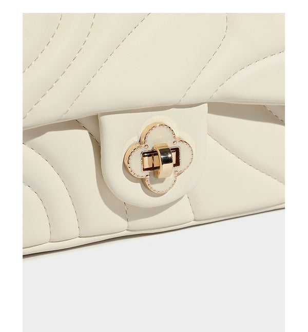 Compact cream quilted flap crossbody bag with wave stitching, gold-tone chain strap, and four-petal turn-lock clasp, detail