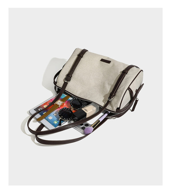 Beige canvas barrel bag with dark brown leather-look trim, silver-tone hardware, top zip closure, and adjustable shoulder