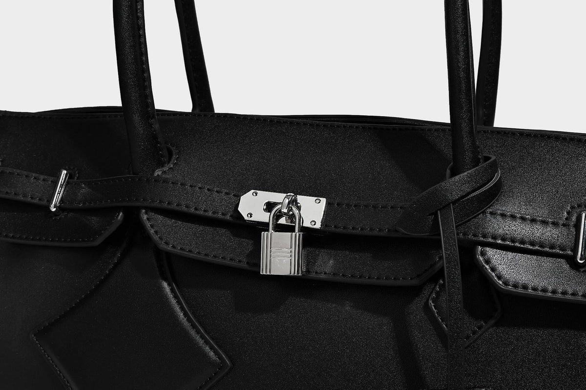 Strukturierte Tote-Bag in schwarzer Lederoptik mit Drehverschluss in Vorhängeschloss-Optik, dekorativen Riemendetails und abgerundeten Doppelhenkeln
