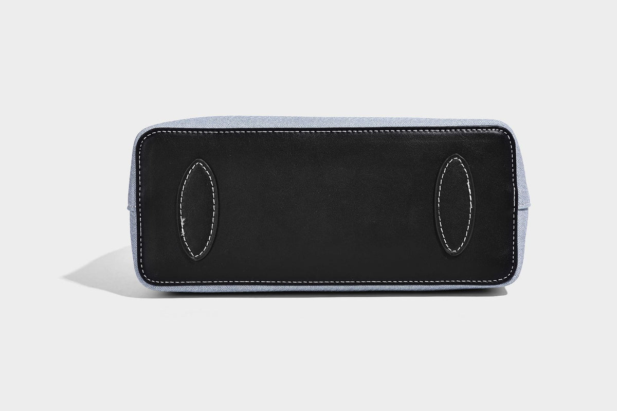 Structured light-blue denim-look tote bag with black leather-look handles, white contrast stitching, silver-tone hardware