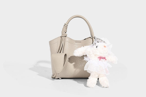 Structured mini tote bag in pebbled leather-look finish with knotted top handles, front flap pocket, and detachable shoulder