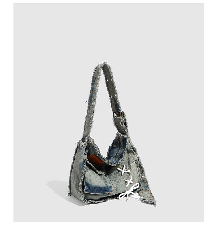 Slouchy distressed denim shoulder bag with frayed edges, white lace-up cross detail, front snap pocket, and long shoulder