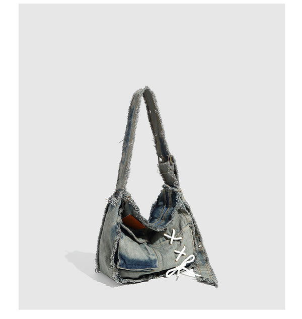 Slouchy distressed denim shoulder bag with frayed edges, white lace-up cross detail, front snap pocket, and long shoulder